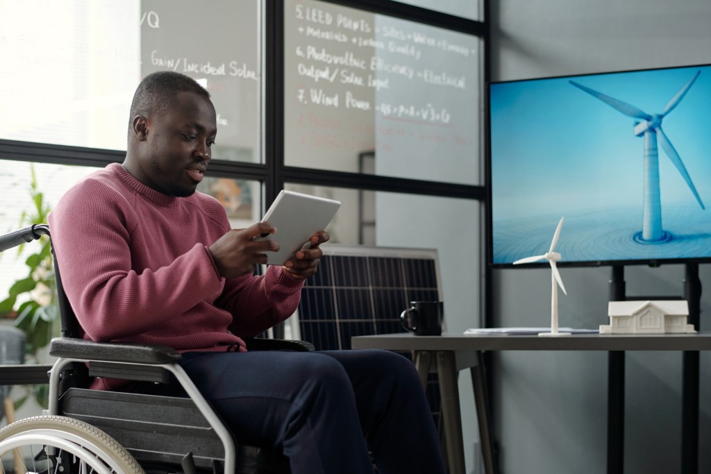Male office worker in wheelchair looking through online data on tablet screen while making presentation in office