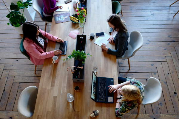Office workers are pictured from above, sitting at a long table and working on laptops